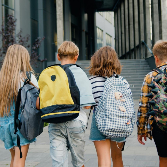 Group of cheerful energetic students child girl boy go to modern campus school with school backpacks. Kids meet each other in front of school. Back to school education kids concept.