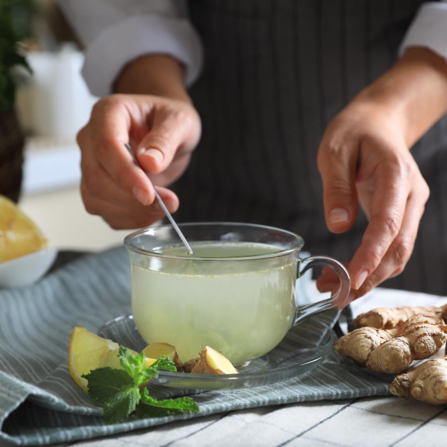 Woman making aromatic ginger tea at table indoors, closeup