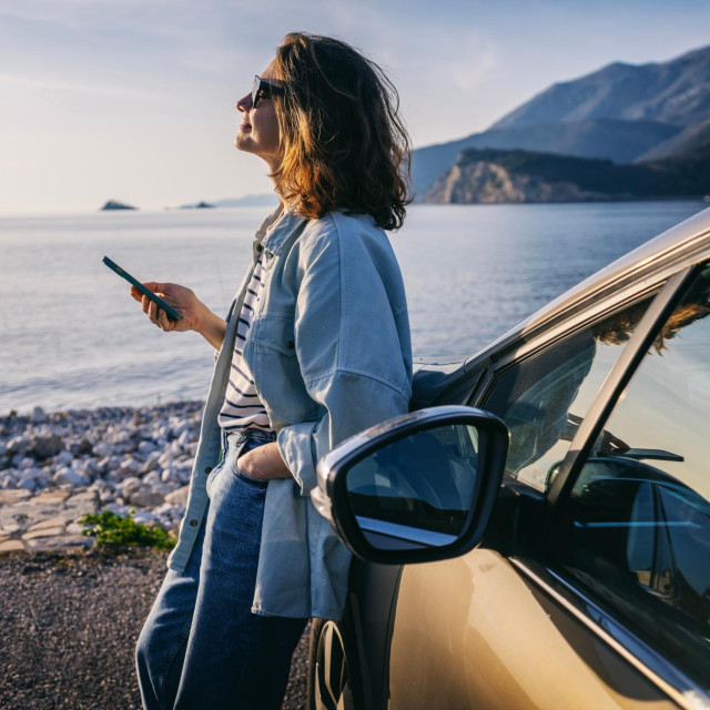 oung woman traveler in a hat standing by her car during summer sea holiday
