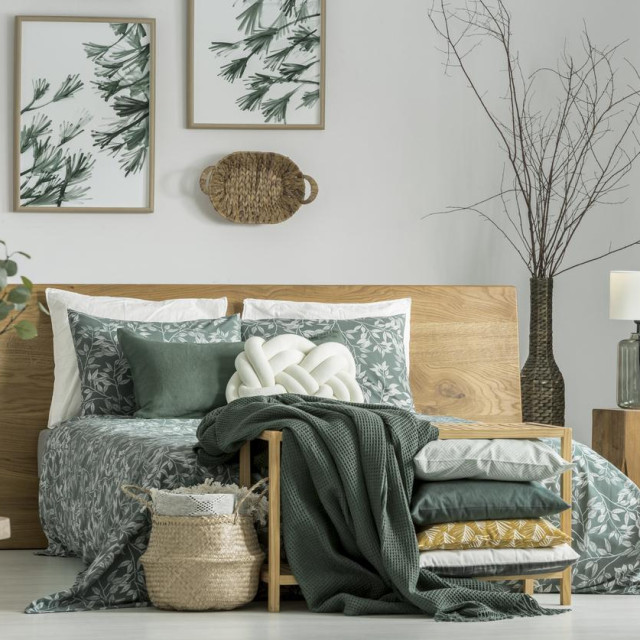 Pillows and blanket on cabinet in khaki bedroom with wooden furniture and white pillow on bed