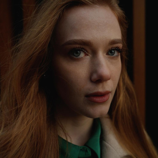Portrait of young beautiful redhead woman looking at cemra pensive - serious, serene, thoughtful concept. Minimum brightness