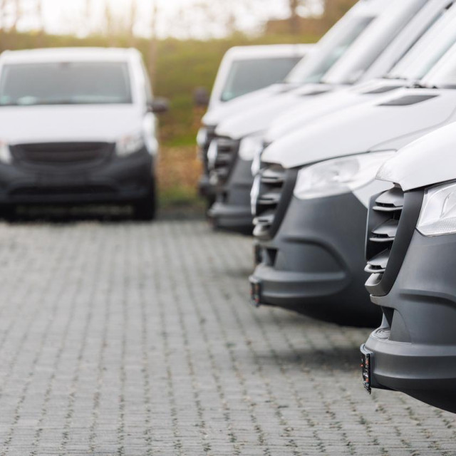 Fleet new modern electric hybrid hydrogen or diesel white vans parked in line row outdoors. Cargo freight industrial courier transportation logistics service. Commercial vehicle maintenance insurance.