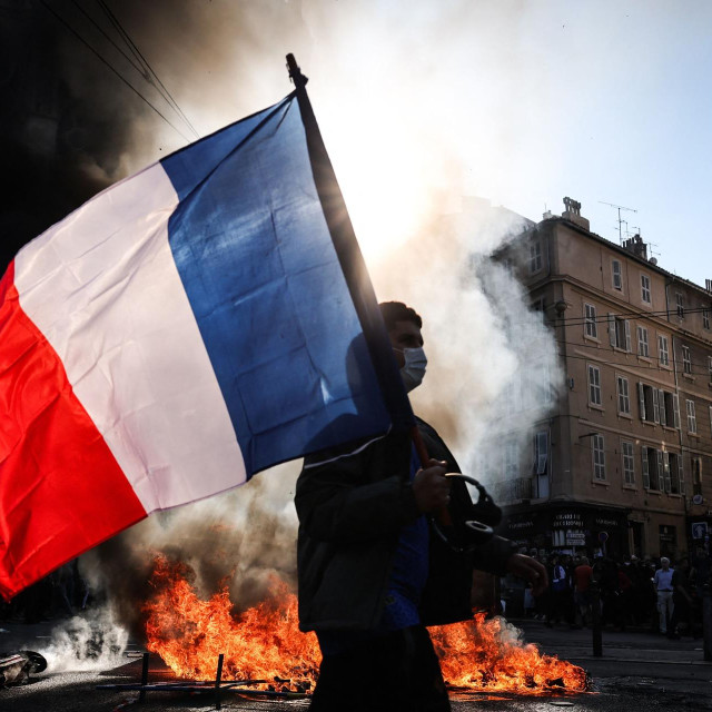 Prosvjednik s francuskom zastavom prolazi pokraj požara u Marseilleu 17. listopada 2026. uoči sukoba na demonstracijama protiv visokih troškova života, organiziranima u sklopu svesavezne mobilizacije koja je okupila bivše ”Žute prsluke”, učenike, studente, klimatske aktiviste i poljoprivrednike