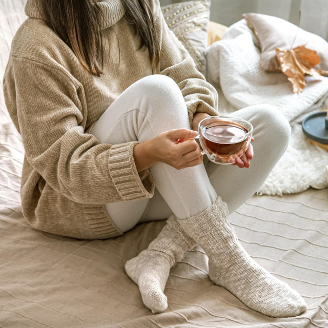 Cozy autumn or winter at home, a woman in a knitted sweater with a Cup of tea and a book.